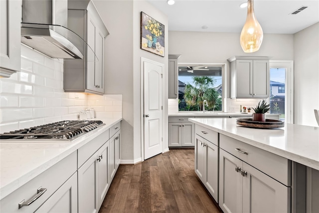 kitchen with hanging light fixtures, wall chimney range hood, dark hardwood / wood-style flooring, backsplash, and stainless steel gas stovetop