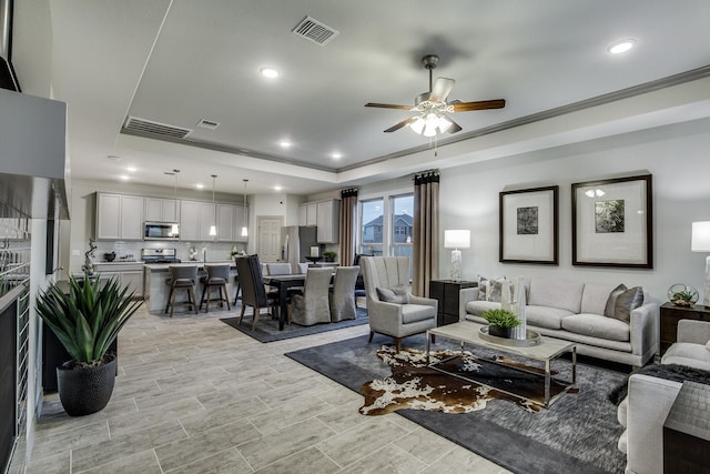 living room with ceiling fan, a raised ceiling, and crown molding