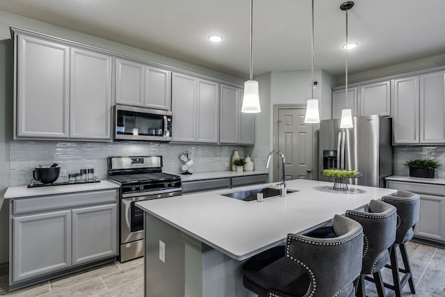 kitchen featuring gray cabinetry, sink, hanging light fixtures, stainless steel appliances, and a kitchen island with sink