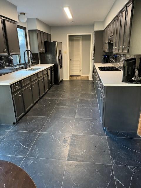 kitchen with tasteful backsplash, sink, stainless steel refrigerator, and black stovetop