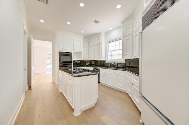 kitchen with paneled built in fridge, a center island with sink, white cabinets, and light hardwood / wood-style flooring