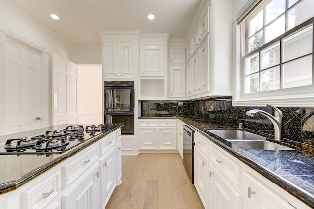 kitchen with appliances with stainless steel finishes, light wood-type flooring, dark stone counters, sink, and white cabinetry