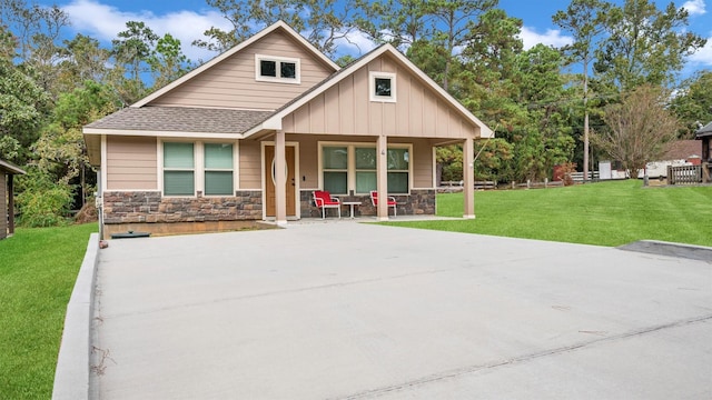 craftsman inspired home featuring roof with shingles, a porch, board and batten siding, a front yard, and stone siding