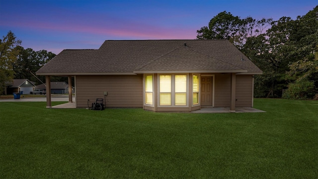 back of property at dusk featuring roof with shingles and a lawn