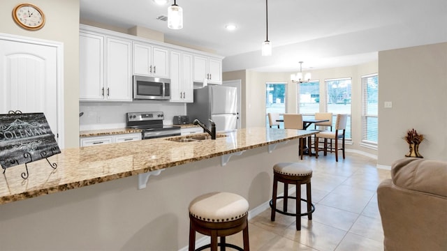 kitchen with light tile patterned floors, white cabinets, appliances with stainless steel finishes, a breakfast bar, and a sink