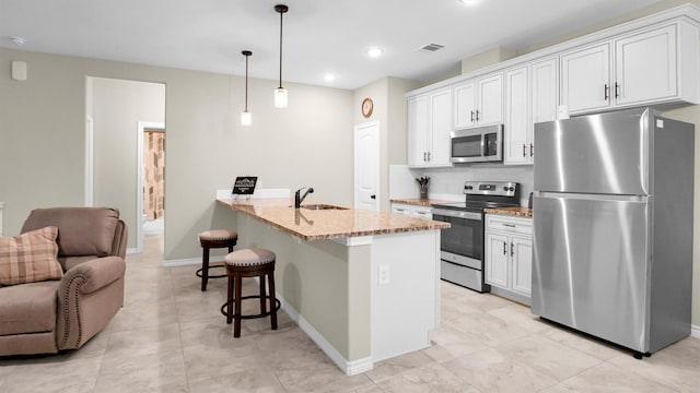 kitchen featuring light stone counters, a breakfast bar area, a sink, visible vents, and appliances with stainless steel finishes