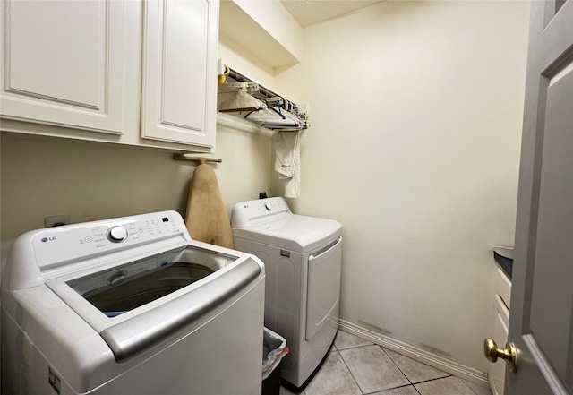 laundry room featuring washing machine and dryer, light tile patterned floors, and cabinets