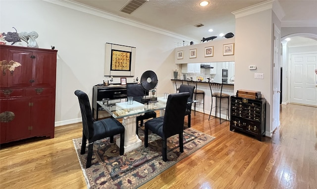 dining room with light hardwood / wood-style floors, a textured ceiling, and ornamental molding