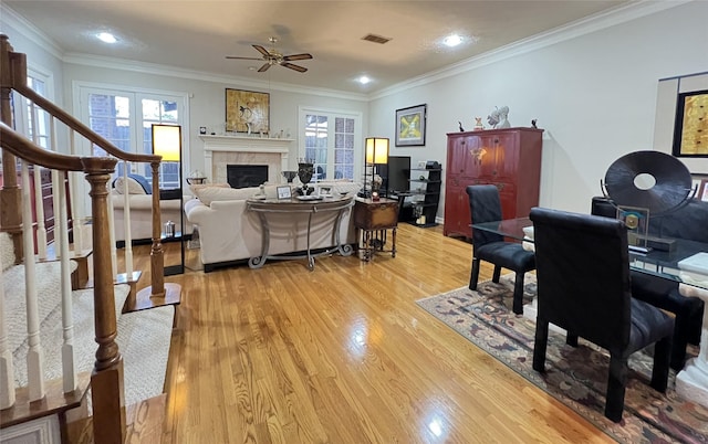 living room featuring ceiling fan, light hardwood / wood-style floors, crown molding, and a tiled fireplace