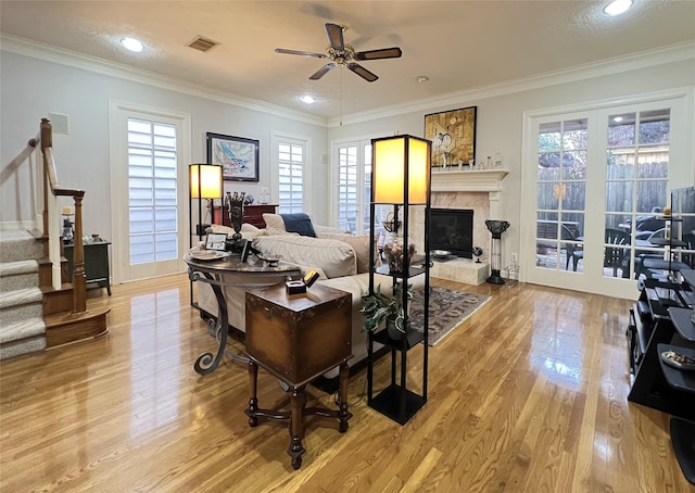 living room featuring ornamental molding, ceiling fan, a healthy amount of sunlight, a tile fireplace, and light hardwood / wood-style floors