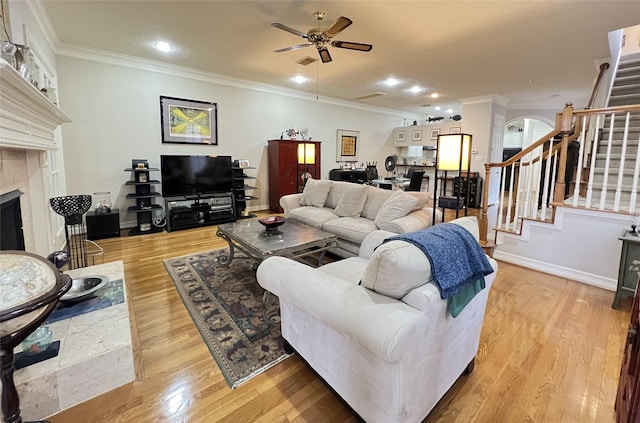 living room with ceiling fan, light wood-type flooring, crown molding, and a tiled fireplace