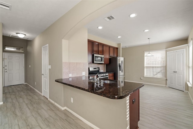 kitchen with dark stone counters, hanging light fixtures, decorative backsplash, kitchen peninsula, and stainless steel appliances