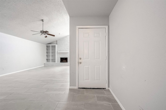 unfurnished living room featuring built in shelves, ceiling fan, a brick fireplace, lofted ceiling, and a textured ceiling