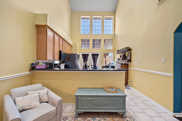 kitchen with kitchen peninsula, black fridge, light tile patterned flooring, and a high ceiling