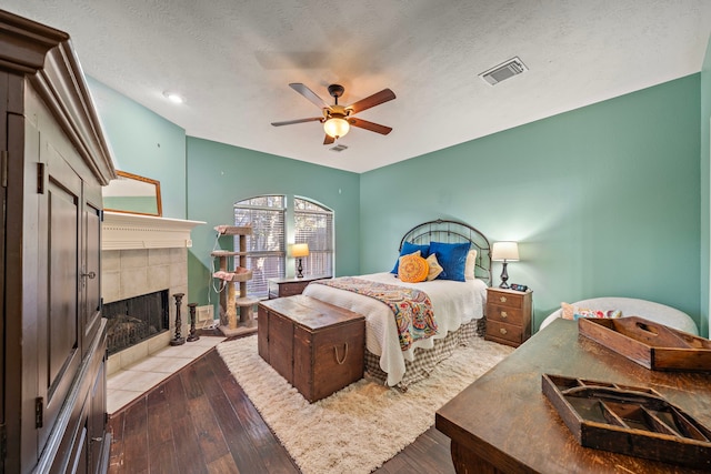 bedroom with a fireplace, a textured ceiling, light wood-type flooring, and ceiling fan