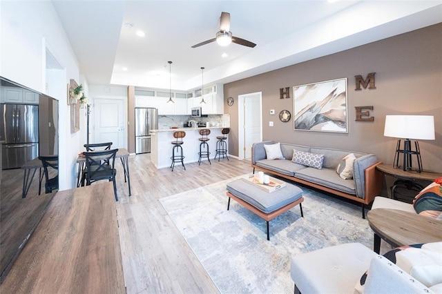 living room with a raised ceiling, ceiling fan, and light hardwood / wood-style flooring