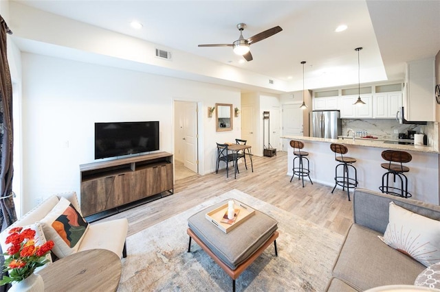 living room featuring light hardwood / wood-style floors, ceiling fan, a tray ceiling, and sink