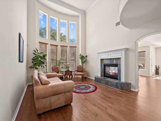 living room with hardwood / wood-style flooring, ornamental molding, a high ceiling, and a tile fireplace