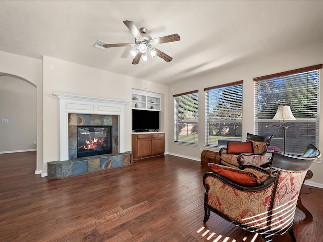 living room with a tile fireplace, dark hardwood / wood-style flooring, built in features, and ceiling fan