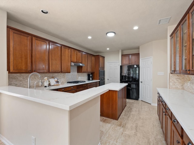 kitchen featuring light stone countertops, a center island, sink, tasteful backsplash, and black appliances