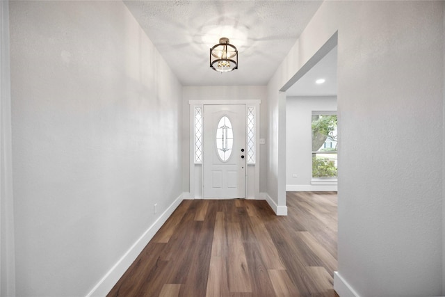 foyer entrance featuring a textured ceiling, dark hardwood / wood-style flooring, and a notable chandelier