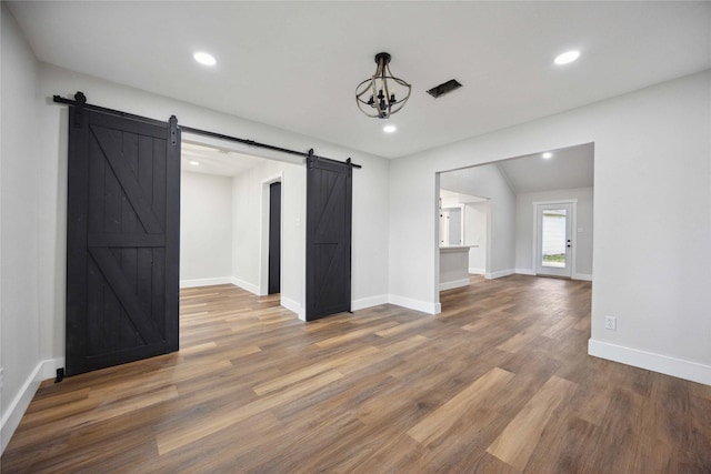 unfurnished room with a barn door, wood-type flooring, and lofted ceiling