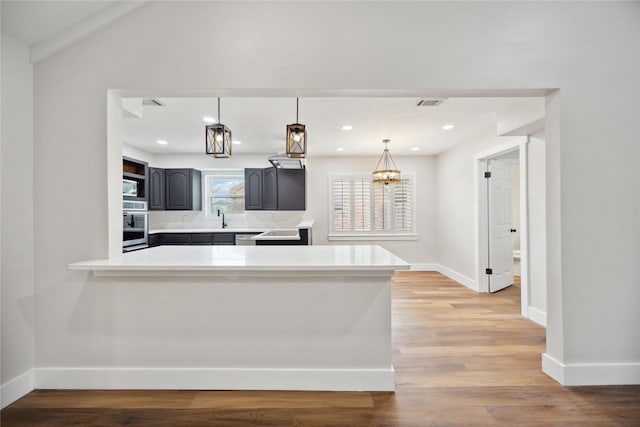 kitchen with kitchen peninsula, stainless steel oven, built in microwave, pendant lighting, and light hardwood / wood-style floors