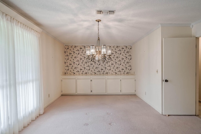 empty room with a textured ceiling, light colored carpet, crown molding, and a chandelier