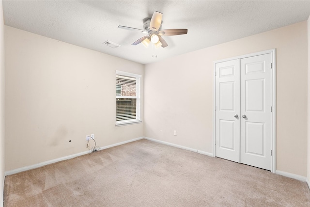 unfurnished bedroom featuring ceiling fan, a closet, light carpet, and a textured ceiling