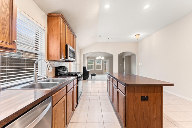 kitchen with light tile patterned flooring, lofted ceiling, decorative backsplash, appliances with stainless steel finishes, and a kitchen island