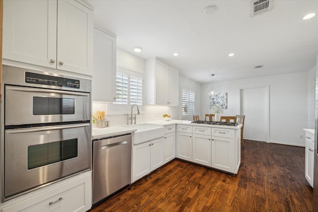 kitchen with kitchen peninsula, dark hardwood / wood-style floors, white cabinetry, and stainless steel appliances