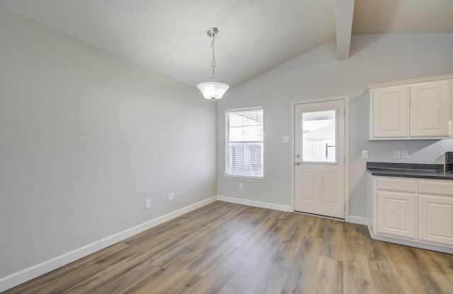 unfurnished dining area featuring lofted ceiling with beams and light wood-type flooring