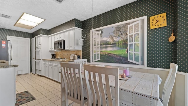 kitchen with a textured ceiling, stainless steel appliances, white cabinetry, and light tile patterned flooring