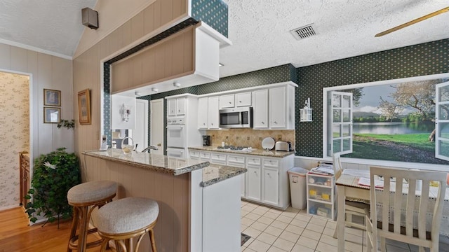 kitchen with white cabinetry, light stone countertops, kitchen peninsula, a textured ceiling, and a breakfast bar