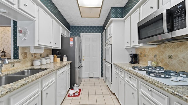 kitchen with white cabinetry, white appliances, sink, and light tile patterned floors