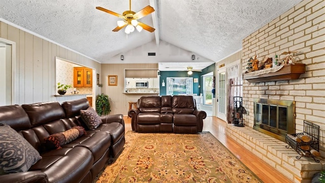 living room featuring a brick fireplace, a textured ceiling, ceiling fan, lofted ceiling with beams, and light hardwood / wood-style flooring