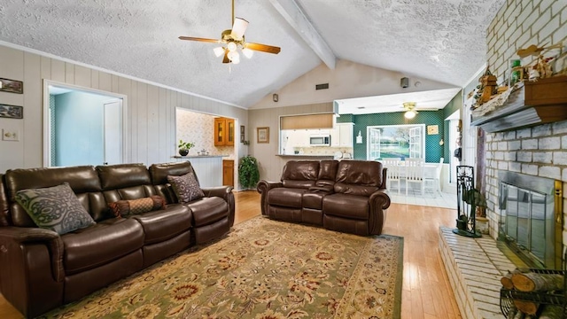 living room with ceiling fan, a brick fireplace, vaulted ceiling with beams, light hardwood / wood-style flooring, and a textured ceiling