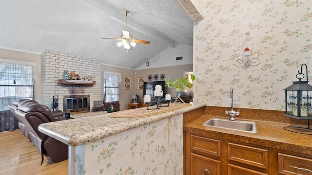 kitchen with ceiling fan, sink, a brick fireplace, kitchen peninsula, and light wood-type flooring