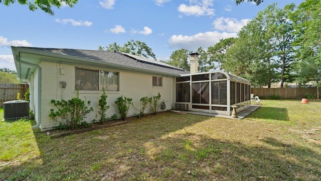 back of property with a lawn, central air condition unit, and a sunroom