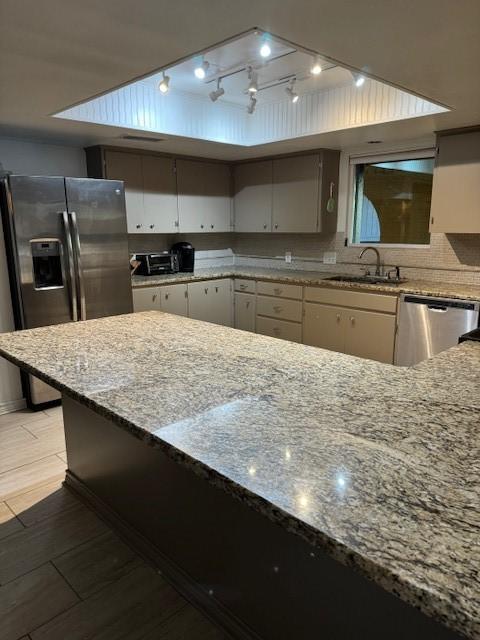 kitchen with appliances with stainless steel finishes, backsplash, light stone counters, sink, and white cabinets