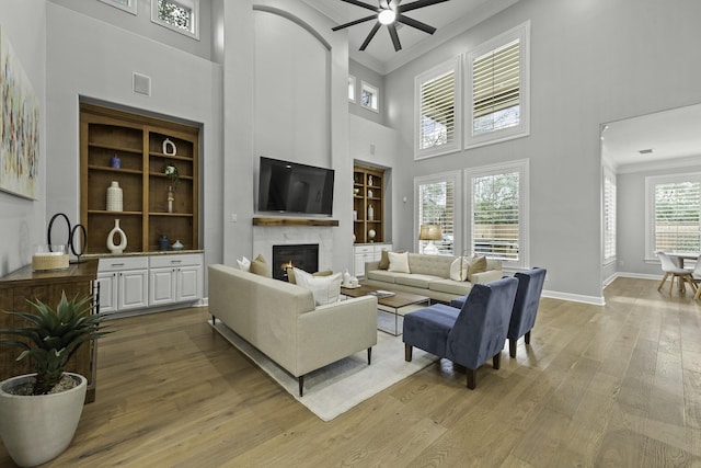 living room with a wealth of natural light, light hardwood / wood-style flooring, crown molding, and built in shelves