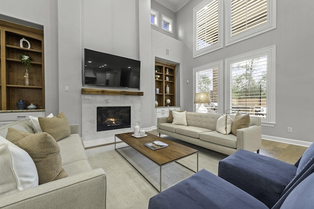 living room featuring light hardwood / wood-style floors, ornamental molding, a fireplace, a high ceiling, and built in shelves