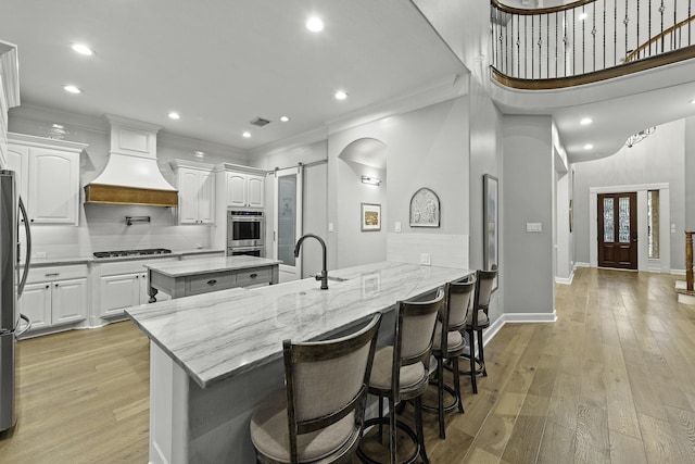 kitchen with white cabinets, light stone counters, custom exhaust hood, a barn door, and appliances with stainless steel finishes