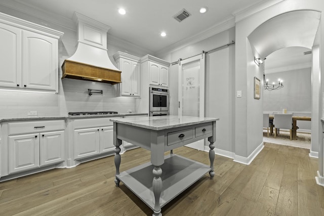 kitchen with white cabinets, light stone counters, light hardwood / wood-style flooring, decorative backsplash, and a barn door