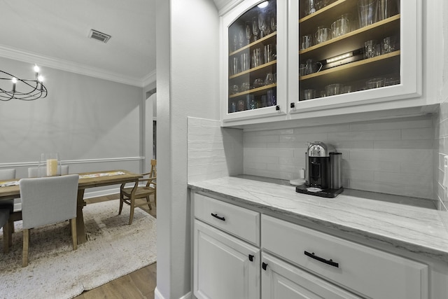 bar with light stone counters, dark hardwood / wood-style floors, tasteful backsplash, crown molding, and white cabinets