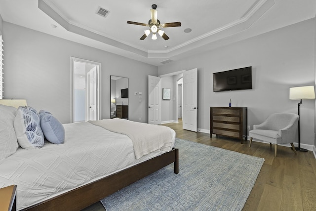 bedroom featuring dark wood-type flooring, a raised ceiling, ceiling fan, and crown molding