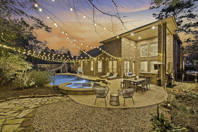 pool at dusk featuring a patio, an in ground hot tub, and a water slide