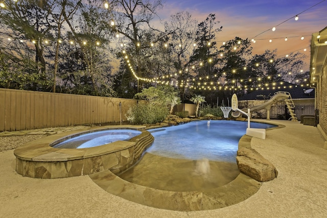 pool at dusk featuring an in ground hot tub and a water slide