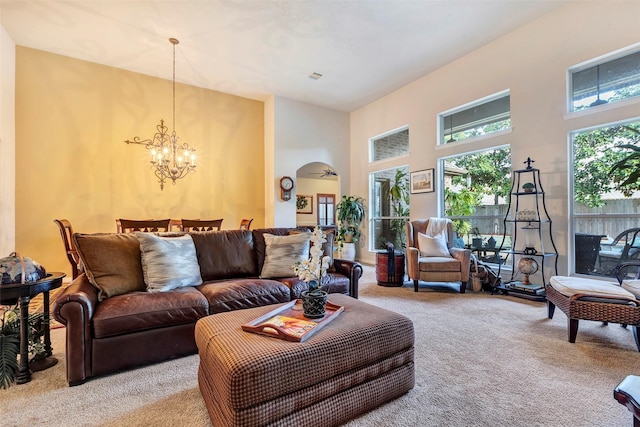 living room with ceiling fan with notable chandelier, light colored carpet, and a high ceiling