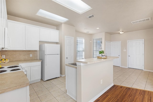 kitchen with white refrigerator, light tile patterned flooring, a center island, and white cabinets